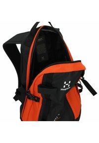 Mochila negra y naranja con compartimentos dobles con cremallera, correas ajustables y un bolsillo frontal. Presenta un logo y una textura de tela resistente.