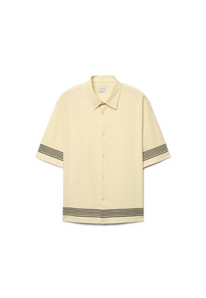 Beiges Kurzarmhemd mit Knopfleiste, schwarzen horizontalen Streifen an den Ärmeln und am unteren Saum, mit spitzem Kragen.