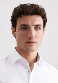 Weißes Hemd mit Spread-Kragen und gemustertem Innenfutter. Glatter Stoff, klassische Knopfleiste, taillierte Passform.