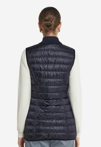 Marinblå, vadderad väst med horisontell quiltad design, lätt material och ribbad krage. Bakifrån visar en slät yta och skräddarsydd passform.