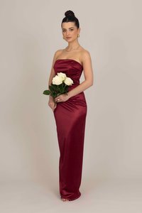 Burgunderfarbene Satin-strapless Abendkleid mit Raffung; Modell hält einen Strauß weißer Rosen; glatte Textur, bodenlanger Schnitt.