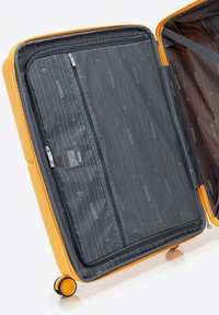 Interno di una valigia gialla rigida con rivestimento in tessuto grigio. Presenta una tasca a zip in rete, divisori decorati e ruote per la mobilità.