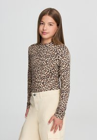 Beżowa, dopasowana bluzka z długim rękawem zdobiona czarno-brązowym wzorem w panterkę. Połączona z kremowymi spodniami cargo z kieszeniami.