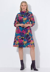 Sukienka w kwiatowy wzór na niebieskim tle, z różowymi, fioletowymi i żółtymi liśćmi. Rękawy 3/4, wysoki kołnierz oraz rozkloszowany dół. W zestawie z fioletowymi botkami za kostkę.