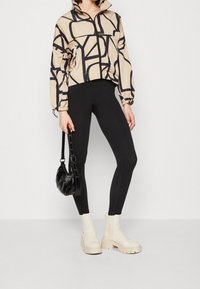 Giacca cropped beige con motivo geometrico nero, abbinata a leggings neri a coste e stivaletti con plateau crema. Una borsa nera completa il look.