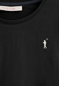 Camiseta de algodón negra con cuello redondo y mangas cortas, con una pequeña figura bordada en blanco sosteniendo un palo de golf en el lado izquierdo del pecho.