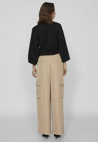 Pantalones cargo de pierna ancha en color beige con bolsillos laterales, tejido texturizado y un ajuste a medida. Combinados con un suéter negro de punto suelto.