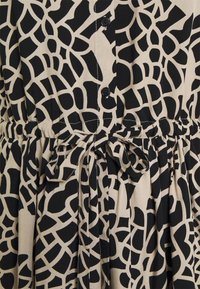 Musta ja beige mekko, jossa on geometrinen kuosi, vyötärösolki, napit ja laskostettu pinta. Kangas näyttää kevyeltä ja sileältä.