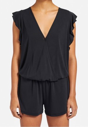 Czarny kombinezon bez rękawów z głębokim dekoltem w kształcie litery V, falbankami na ramionach, elastyczną talią i luźnymi szortami na stojącej osobie.