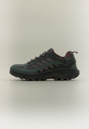 Dunkelgrüner und brauner Merrell Wanderschuh mit Mesh- und Veloursleder-Obermaterial, dicker profillierter Sohle und Schnürverschluss, Seitenansicht vor neutralem Hintergrund.