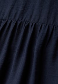 Mörkblått tyg med en mjuk textur, som har vertikala veck vid sömmen som skapar subtil volym och rörelse.