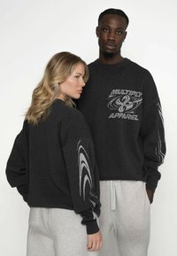 Hanorace supradimensionate de culoare gri închis, cu designuri grafice intricate argintii pe mâneci și piept, asortate cu pantaloni de trening gri deschis.