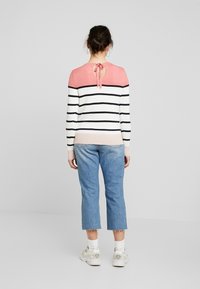 Randig tröja med en rosa och vit färgkombination, med en detalj med knytning på baksidan. Bärs med korta blå jeans och vita sneakers.