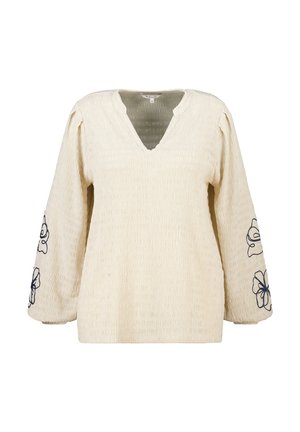 Blouse à manches longues de couleur crème avec un col en V et une broderie florale bleu marine sur les manches.