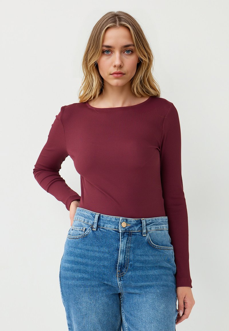Maglietta borgogna a coste con maniche lunghe abbinata a jeans in denim azzurro chiaro a vita alta. La maglietta ha un collo rotondo, una silhouette aderente e una texture morbida.
