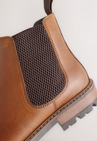 Bottes Chelsea en cuir marron avec panneau latéral élastique foncé et languette, présentant des détails cousus et une semelle robuste en gros plan.