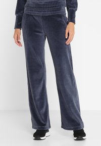 Navy Velours-Trainingshose mit entspannter Passform, elastischem Bund und weichem Material, kombiniert mit schwarzen Sportschuhen.