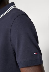 Polo shirt blu navy con tessuto testurizzato, colletto classico con strisce bianche e un piccolo dettaglio con logo tricolore sulla manica.