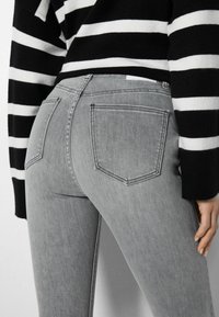 Jeans de mezclilla gris con un diseño ajustado. Presenta dos bolsillos traseros y una textura suave. Combinados con un suéter de rayas en blanco y negro.
