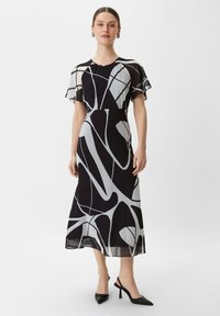 Czarna i biała sukienka z abstrakcyjnym wzorem, krótki lekko opadający rękawek, dopasowana talia, długość do kostek i lekką tkaninę. Czarne szpilki w akcentach.