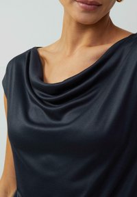 Top s cowl krkem z hladké, tmavě námořnické látky; obsahuje jemné drapérie, krátké rukávy a přiléhavý střih, který akcentuje výstřih.