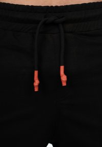 Zwarte joggingsbroek met een elastische tailleband, voorzien van een trekkoord met heldere oranje uiteinden; gladde textuur en details met zijzakken.