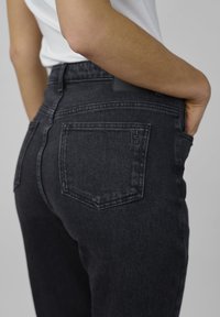 Svarta denimjeans med hög midja, med bakfickor och subtil sömnad. Materialet verkar ha en texturerad yta med en lätt stretch.