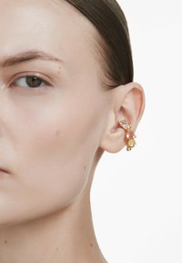 Gold ear cuff featuring colorful gemstones in various shapes, positioned along the outer edge of the ear, with a delicate design and shiny finish.