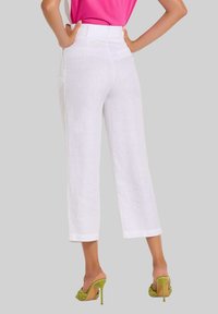 Weiße Leinen-Cropped-Hosen mit tailliertem Bund und geradem Bein-Design. Kombiniert mit grünen High-Heel-Sandalen.