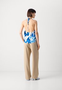 Haut halter à motifs bleus et blancs avec un dos nu, associé à un pantalon large beige et des sandales bleu clair. Texture de tissu lisse.