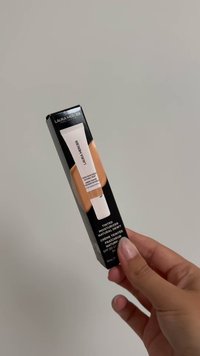 Laura Mercier getinte moisturizer in een witte tube met een zwarte doos. De tekst geeft aan dat het 'Natuurlijk Glanzend' is, SPF 30, 15 ml, met een zachte afwerking.