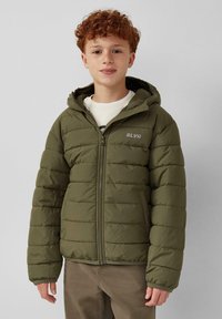 Olivgrüne, gepolsterte Jacke mit Kapuze, Reißverschluss und elastischen Bündchen. Mit dem Logo "SLVR" auf der Brust. Über einem weißen T-Shirt getragen.