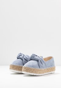 Ljust blå mocka espadrillos med knutdetalj på toppen och flätad jute plattformssula med vit gummiyttersula.