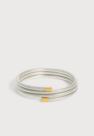 Ευέλικτο ασημένιο βραχιόλι με τρεις θηλιές και χρυσούς τελείωμα σε λευκό φόντο.