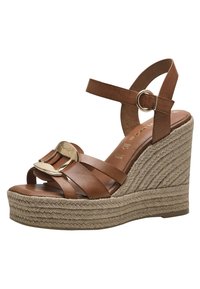 Sandale compensée en cuir marron avec des lanières entrecroisées, boucle en accent doré et plateforme en jute. Texture lisse, design à bout ouvert.