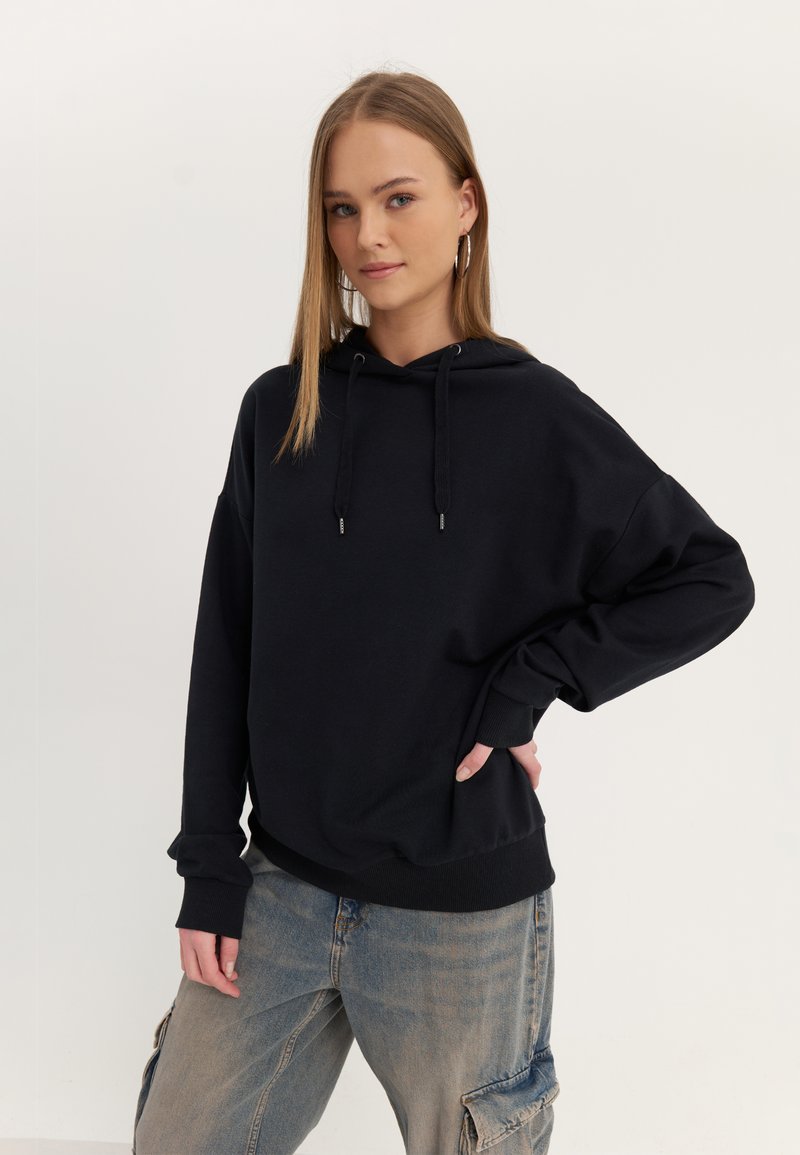 Black hooded sweatshirt with loose fit, ribbed cuffs, and side pockets. Paired with light blue cargo pants featuring side pockets.