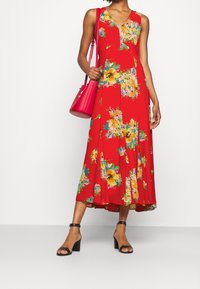 Röd blommig klänning med V-ringning, ärmlös design och plisserade detaljer. Matchas med svarta öppna klackskor och en rosa handväska.