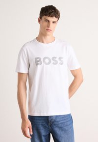 Witte katoenen t-shirt met een grijs gestreepte "BOSS" tekstgrafiek. Het shirt heeft een ronde hals en korte mouwen. Gemaakt met blauwe jeans.