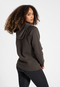 Mörkbrun hoodie med en åtsittande design, dragsko i huvan och ribbade cuffs. Kombineras med svarta leggings, vilket visar en avslappnad och casual look.