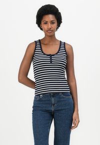 Top de alças às riscas azul-marinho e brancas com decote redondo, apresentando três botões na frente. Combinado com jeans azul de cintura alta.