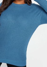 Stickad blå tröja med rundad halsringning, ribbade ärmslut och nederkant, med ett strukturerat vävmönster genom hela plagget.