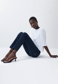 T-shirt blanc oversize, jeans slim-fit bleu foncé et sandales à talons noires à lanières. Tissu lisse avec des détails de couture minimal.