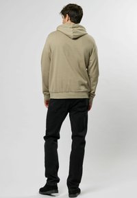 Beige hoodie met een trekkoord en geribbelde onderrand, gecombineerd met zwarte broek met achterzakken. Gemaakt van een zachte katoenmix.