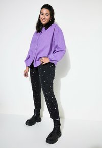 Camicia button-up viola con tessuto testurizzato, abbinata a pantaloni neri con dettagli in perle bianche e stivali neri chunky.