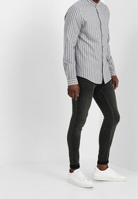 Camicia a righe grigia e bianca, abbinata a jeans skinny scuri e sneakers bianche. La camicia presenta un colletto alla band e maniche lunghe.