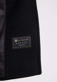 Czarny wełniany płaszcz z gładką podszewką. Posiada prostokątną metkę z logo w złotym i białym kolorze, z napisem "Wool Collection Makalu."