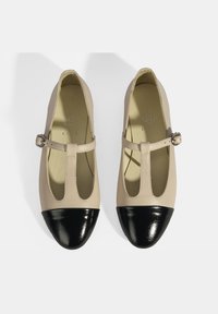 Beige Leder Ballerinas mit schwarzen Lackleder-Spitze, ausgestattet mit einem T-Riemen-Design und seitlichem Schnallenverschluss. Glatte Textur.