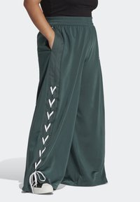 Široké tepláky v tmavě modrozelené barvě, vyrobené z hladké tkaniny. Mají bílé šňůrkové detaily po stranách a elastický pas.