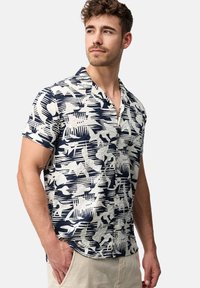 Camisa de manga corta en un tejido ligero, con un patrón abstracto en azul marino y crema, cuello con muesca y cierre de botones en la parte delantera.
