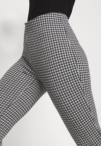 Svartvit houndstooth-mönstrade leggings med hög midja och slät textur, åtsittande design som framhäver benen.